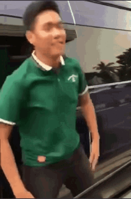 a man in a green shirt is standing in front of a black car
