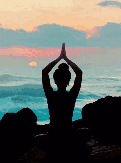 a silhouette of a woman sitting in a lotus position with her hands together
