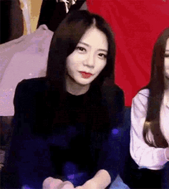 a woman with long black hair is sitting next to another woman on a couch and looking at the camera .
