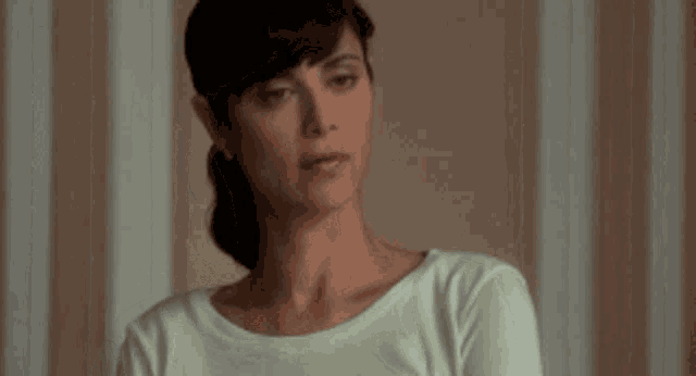a woman in a green shirt is looking at the camera with a striped wall in the background .
