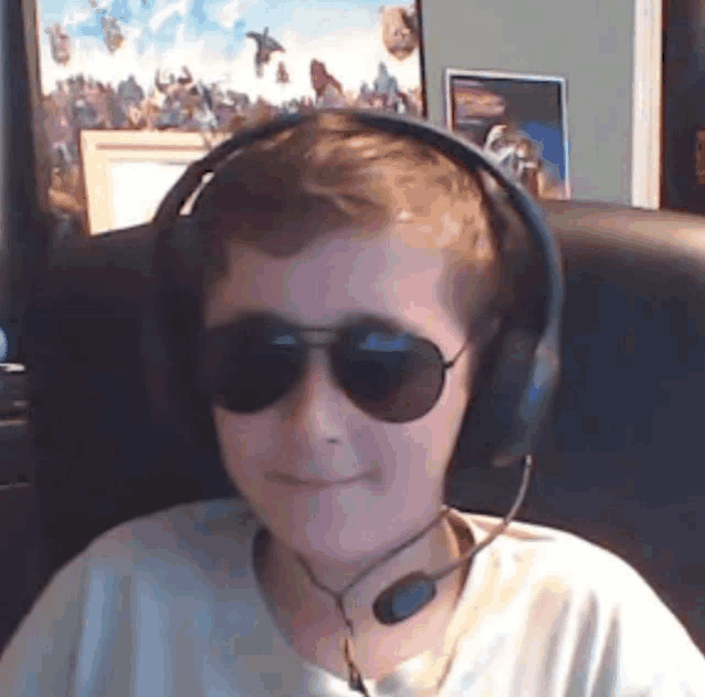 a young boy wearing headphones and sunglasses is sitting in front of a computer screen .