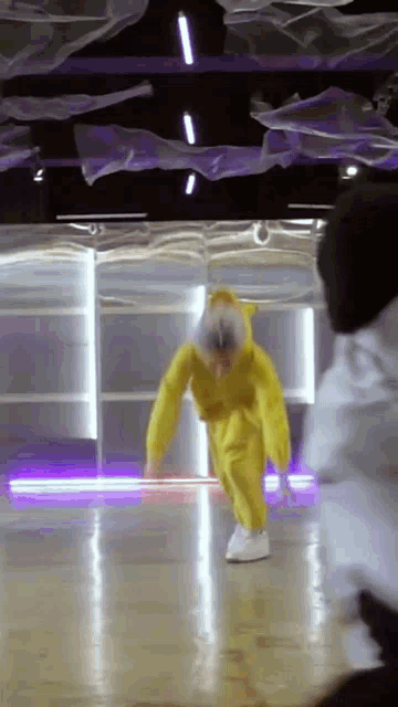 a person in a yellow suit is dancing in a room with purple lights .