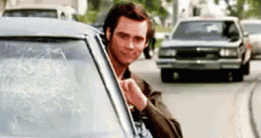 a man is sticking his head out of a car window while a car is driving by .