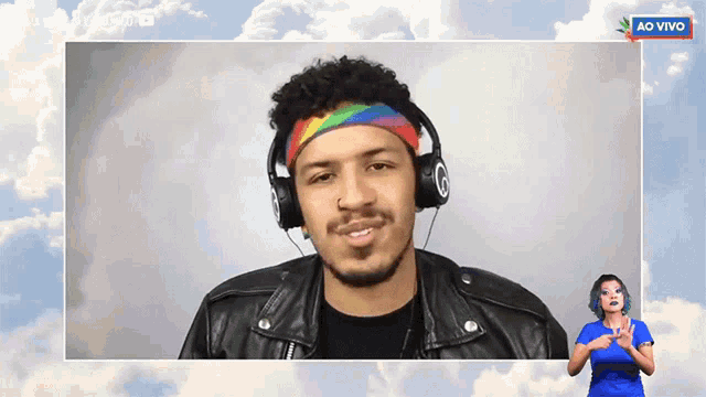 a man wearing headphones and a rainbow headband looks at the camera with a sign that says ao vivo in the background
