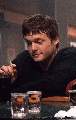 a man is smoking a cigarette while drinking a shot glass of whiskey