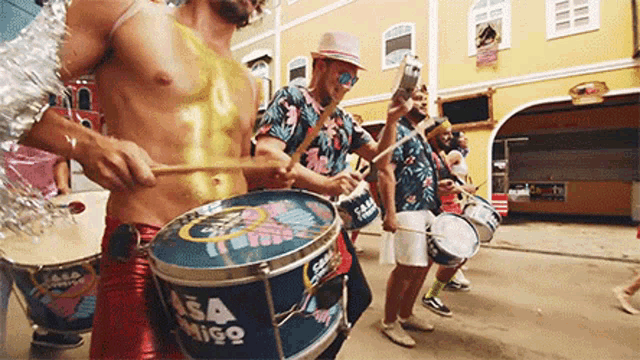 a group of men are playing drums in a parade and one of their drums says asamigo on it .
