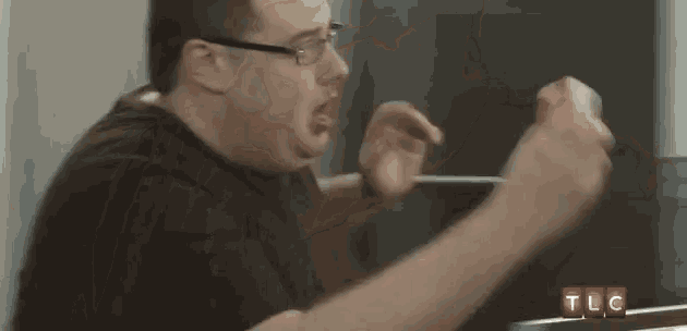 a man with glasses is making a funny face while sitting at a table in front of a tlc sign .