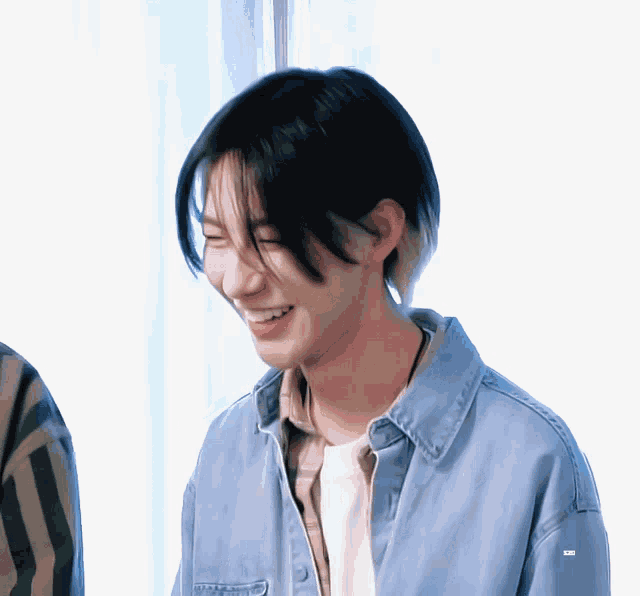 a young man wearing a blue denim jacket and a white shirt smiles