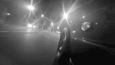 a black and white photo of a car driving down a highway at night .