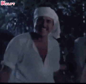 a man wearing a head scarf and a white shirt is standing in the dark .