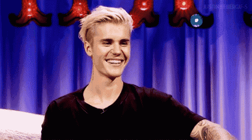 justin bieber is smiling while sitting in front of a blue curtain on a stage .