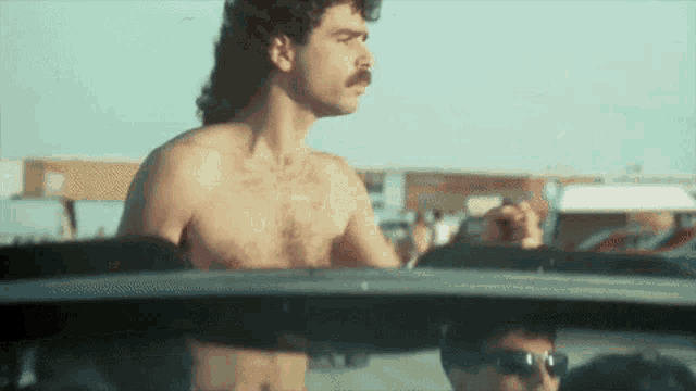 a shirtless man with a mustache is driving a car ..