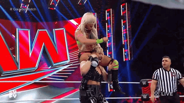 a wrestler is carrying another wrestler on her shoulders during a wrestling match .