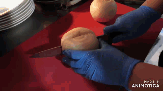 a person wearing blue gloves cuts an onion on a red cutting board