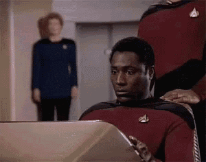 a man in a red shirt is sitting in front of a computer monitor .