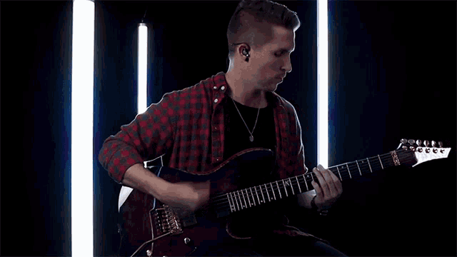 a man in a plaid shirt is playing a guitar that says ibanez on it