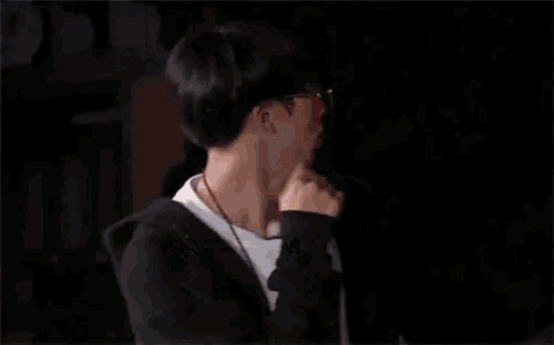 a young man wearing glasses and a black hoodie is standing in a dark room .