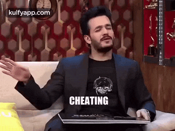 a man in a suit is sitting on a couch with a laptop and a t-shirt that says `` cheating ''