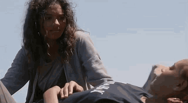 a woman is putting her hand on a man 's chest while he is laying on the ground .