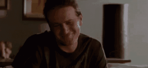 a man in a black shirt is sitting at a table in a living room and smiling .