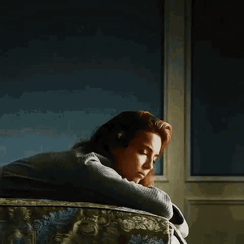 a woman is sitting on a couch with her head on her arms .