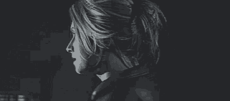 a black and white photo of a woman in a dark room looking at the camera .