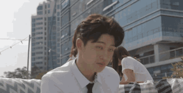a man in a white shirt and tie is sitting in front of a building