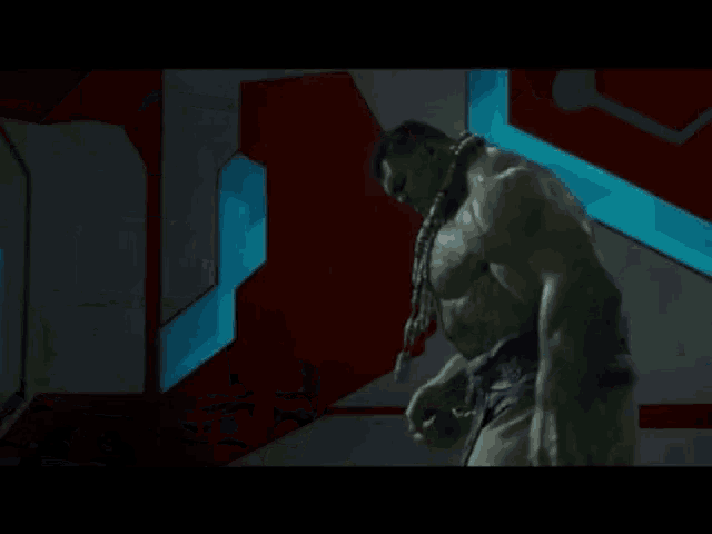 a hulk is standing in a room with a blue light behind him .