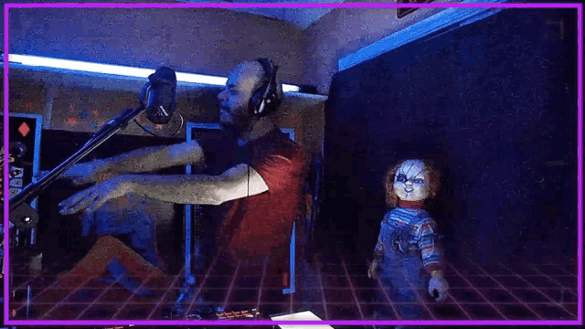 a man wearing headphones is playing a guitar in front of a microphone while a doll is standing next to him .