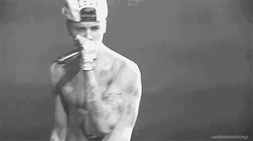 a black and white photo of a shirtless man in a baseball cap holding his chest .