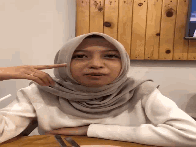 a woman wearing a hijab is sitting at a table with her hand on her face