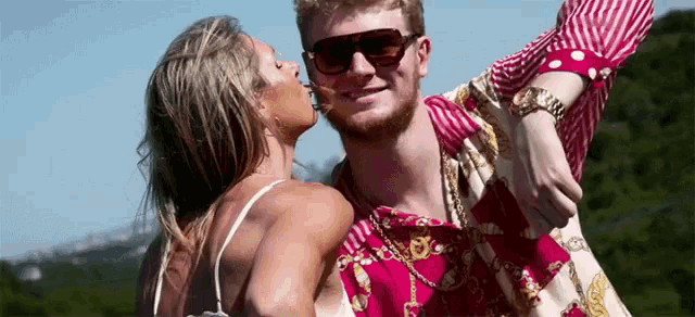 a woman kisses a man on the cheek while he wears sunglasses