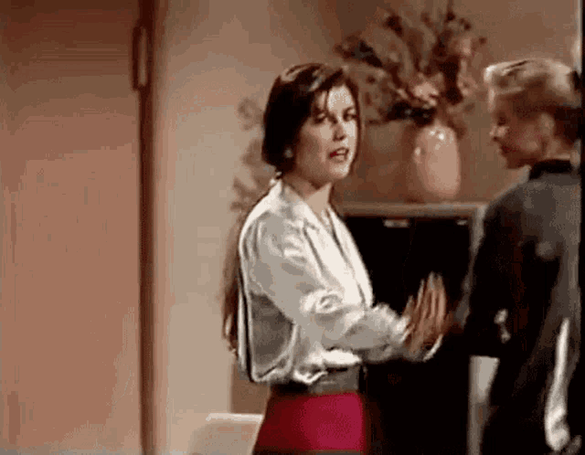 two women are standing next to each other in a room and talking .