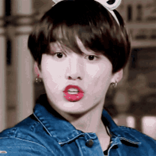 a young man wearing a bunny headband and a denim jacket is making a face .