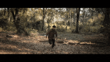 a man in a brown shirt is running through a wooded area