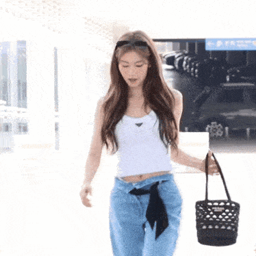 a woman wearing a white tank top and blue jeans is holding a black bag .