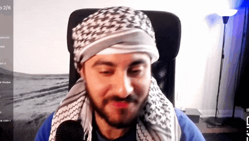 a man wearing a head scarf is sitting in front of a screen that says 2/6 on it