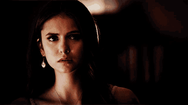 a woman wearing a necklace and earrings looks at the camera
