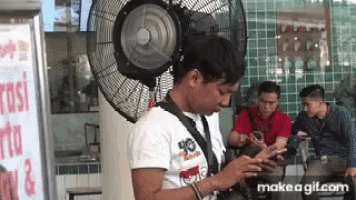 a man is looking at his phone while standing in front of a fan