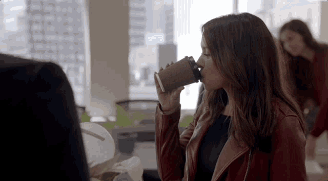 a woman in a red leather jacket drinking from a cup