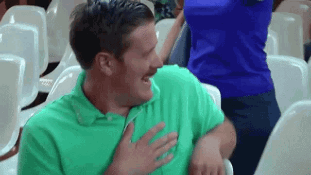 a man in a green shirt is laughing in a crowded stadium