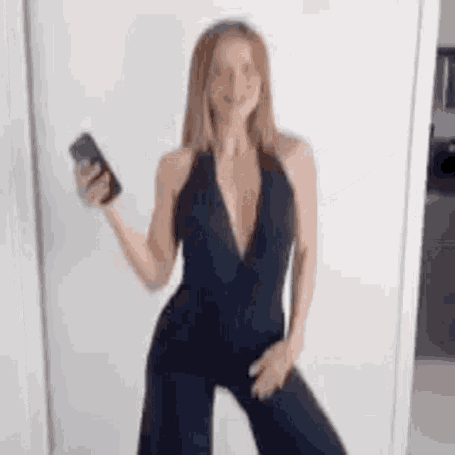 a woman in a black jumpsuit is holding a cell phone and dancing .