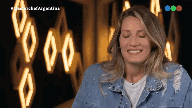 a woman in a denim jacket is smiling in front of a sign that says " masterchef argentina "