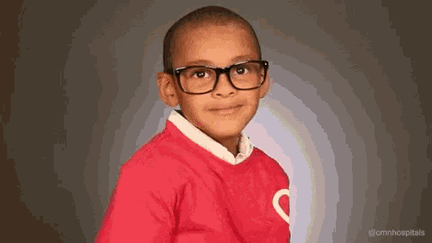 a young boy wearing glasses and a red sweater with a heart on it is smiling .