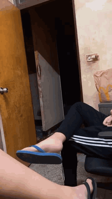 a person wearing flip flops sits on another person 's lap in a room