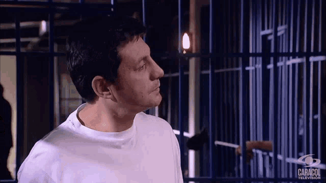 a man in a white shirt is standing in front of a prison cell with caracol television written on the bottom