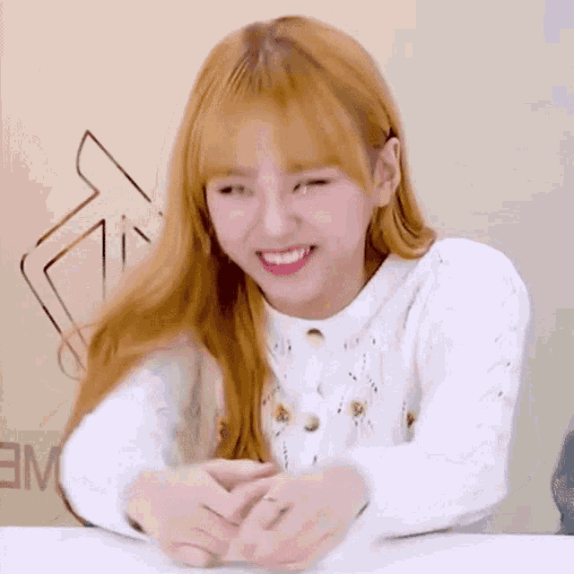 a girl with blonde hair is sitting at a table with her hands folded .
