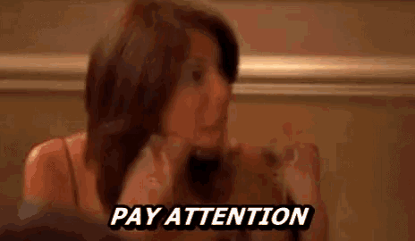 a woman is sitting at a table with a sign that says `` pay attention '' on it .