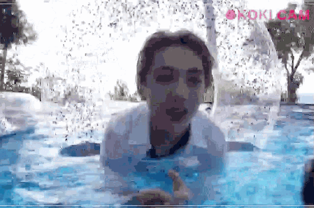 a man in a white shirt is swimming in a pool with a fountain in the background and the word kokicam on the bottom