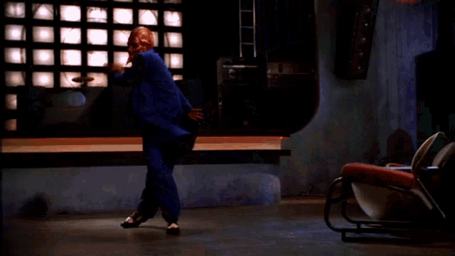 a man in a blue suit is dancing in front of a wall of televisions